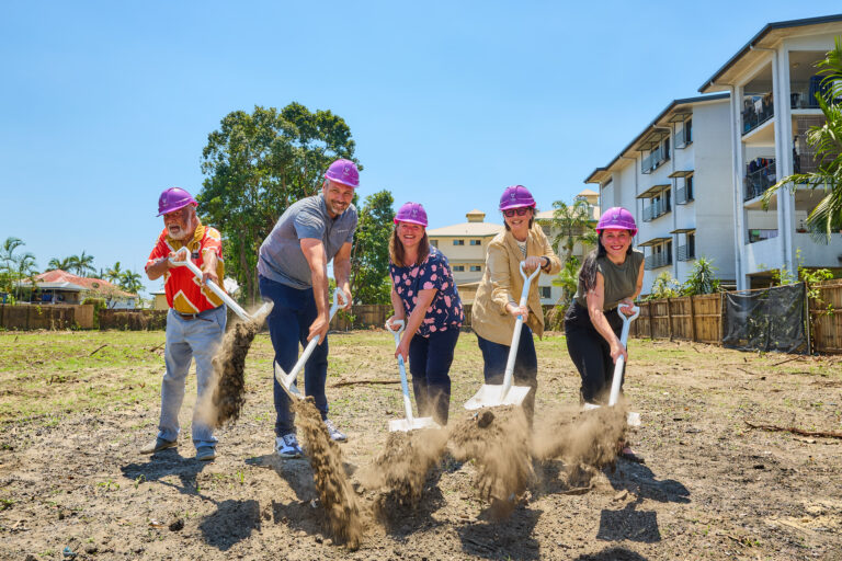 Five people breaking ground with shovels on a construction site.
