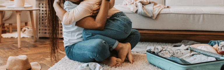 A mother hugging her child next to a half full suitcase