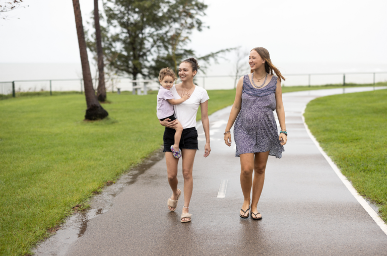 Two smiling young women walking down the Darwin foreshore, one carrying a toddler